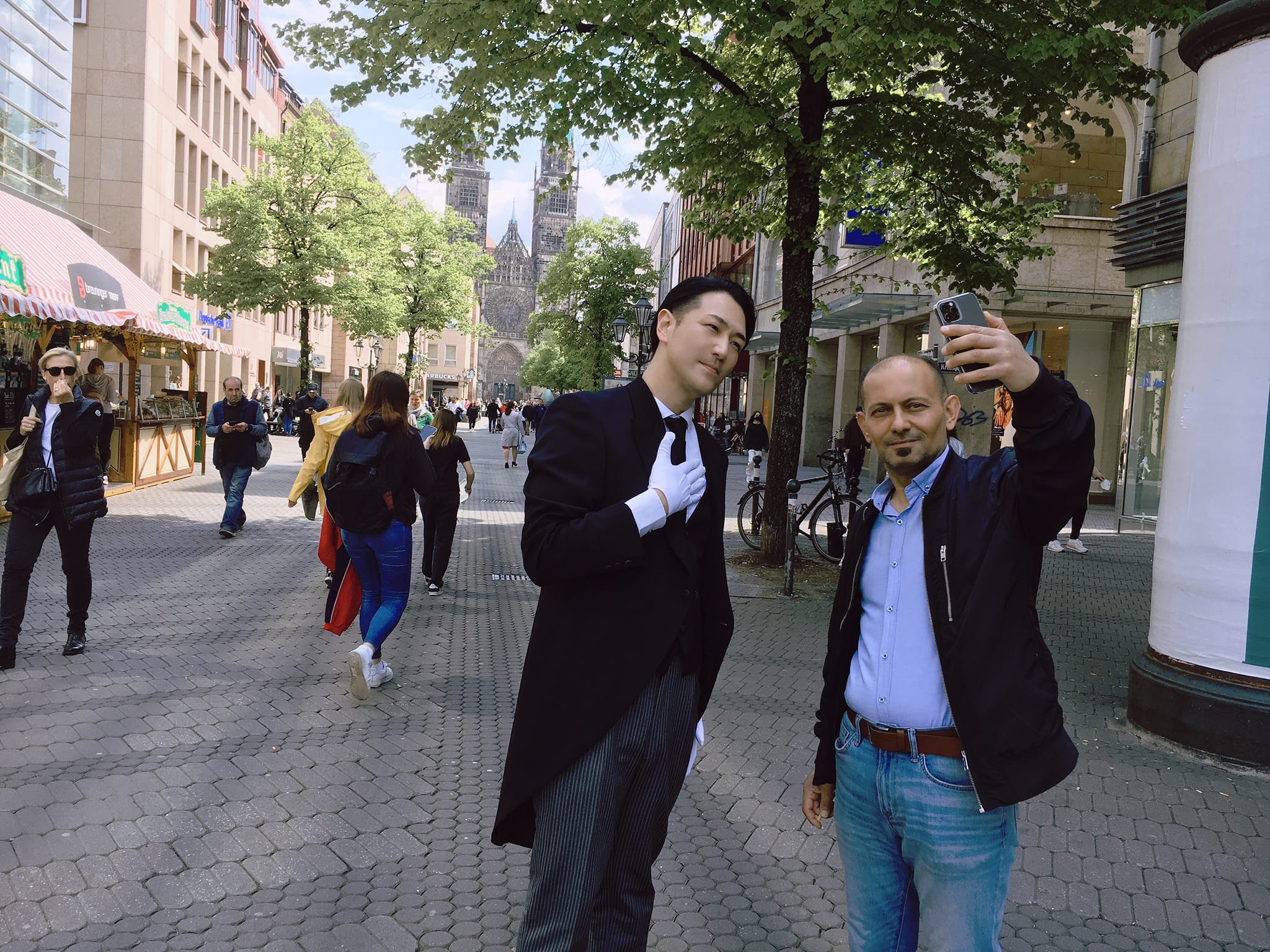 Yuichi Ishii taking a selfie with a fan on a German street, dressed in a slim suit
